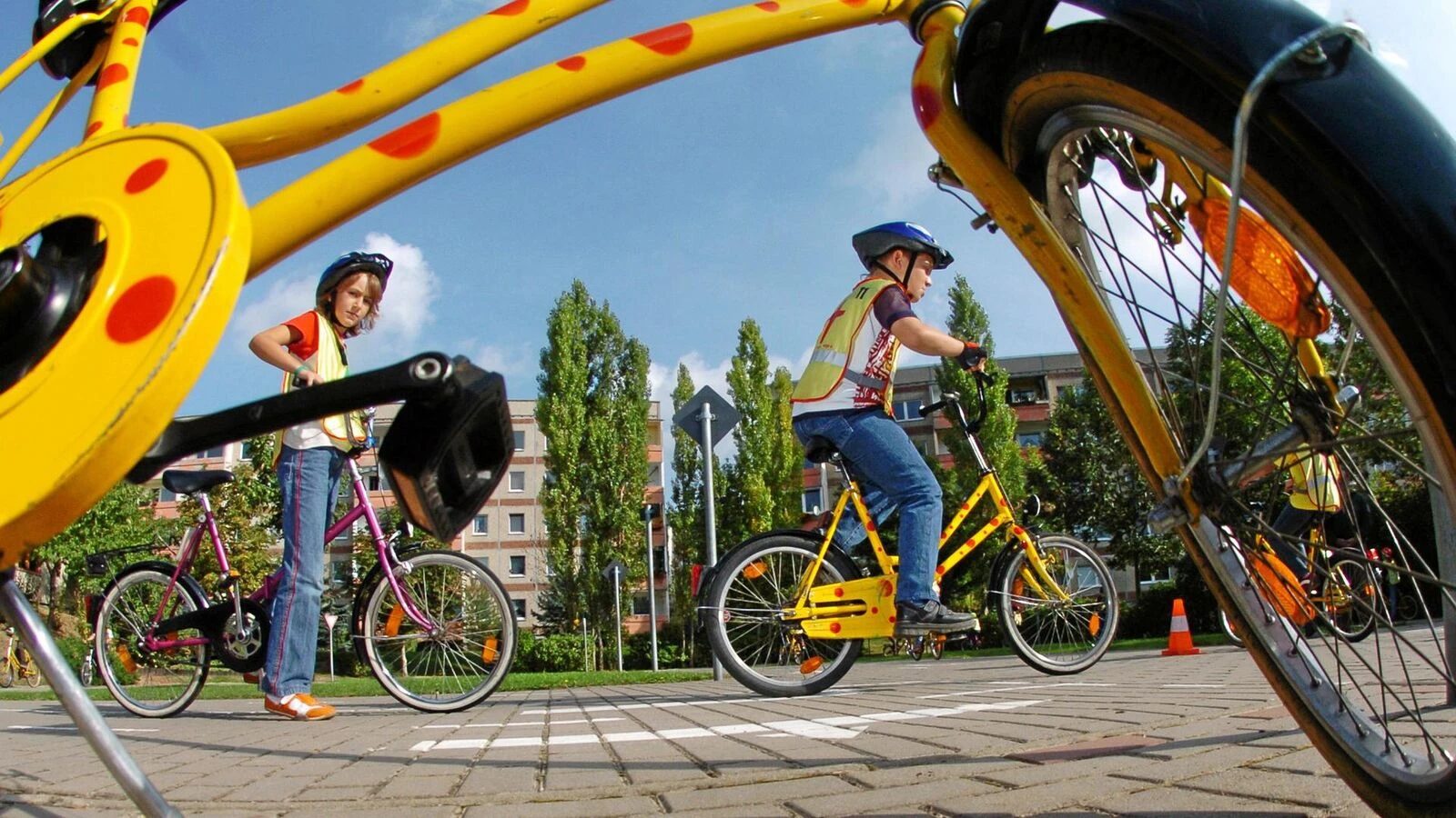 Kinder mit Helm und Warnweste üben auf dem Verkehrsübungsplatz Radfahren